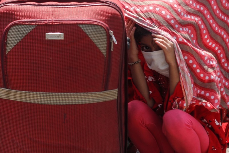 A girl takes shelter under a woman's shawl as they wait in a queue outside a railway station to board a train to their home state of Uttar Pradesh, during an extended lockdown to slow the spreading of the coronavirus disease (COVID-19), in Mumbai. REUTERS/Francis Mascarenhas